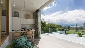 Une cuisine moderne avec des meubles blancs, un coin repas avec une table et des chaises, et un balcon offrant une vue sur le paysage.