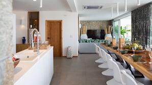 Une cuisine moderne dotée d’un îlot central, d’un coin repas avec une longue table en bois et d’une grande fenêtre agrémentée de rideaux.