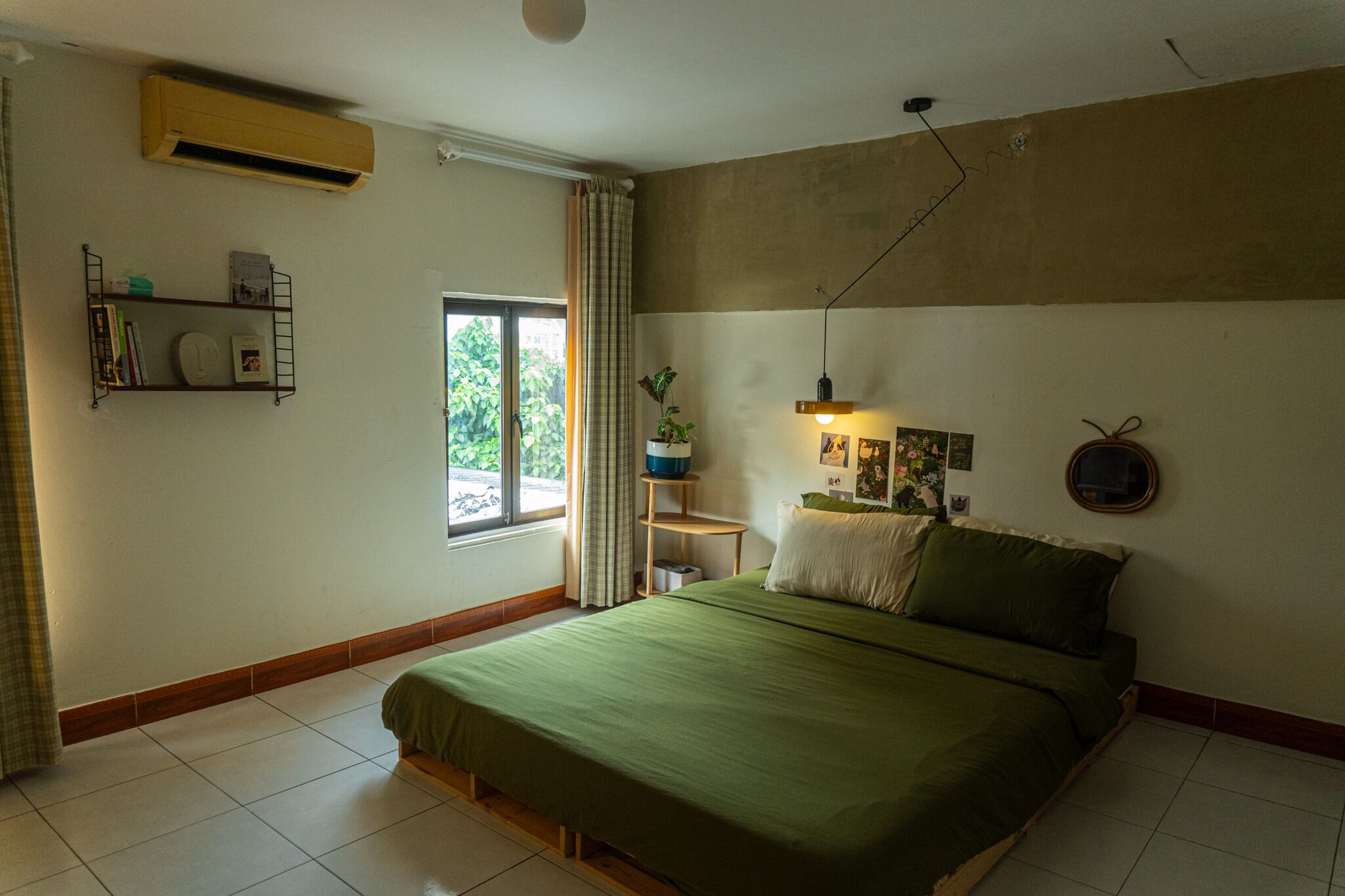 Quarto com cama, prateleira de livros, janela e ar condicionado.