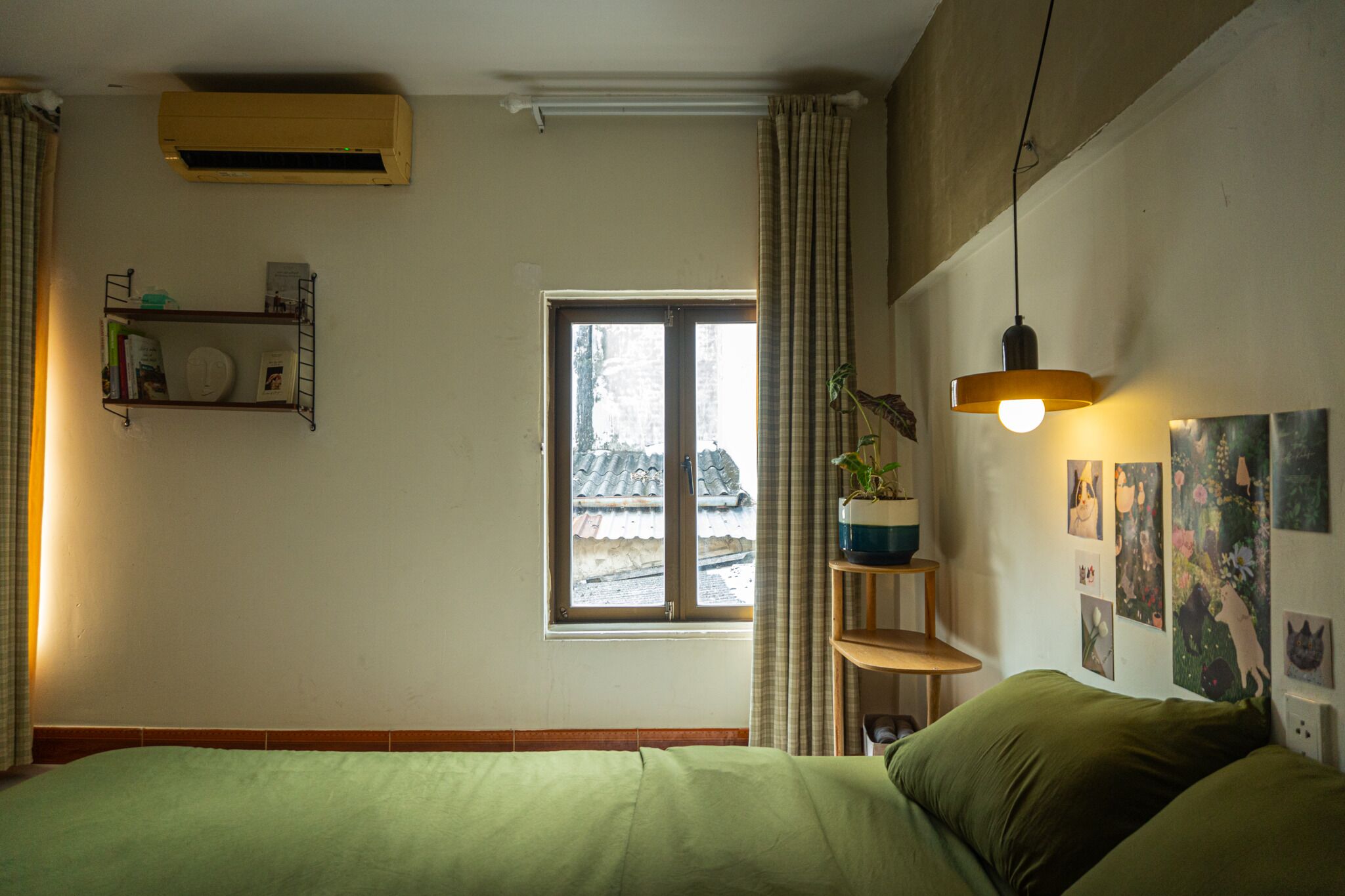 A bedroom with a bed, a window, a shelf with toiletries, and a hanging light fixture.