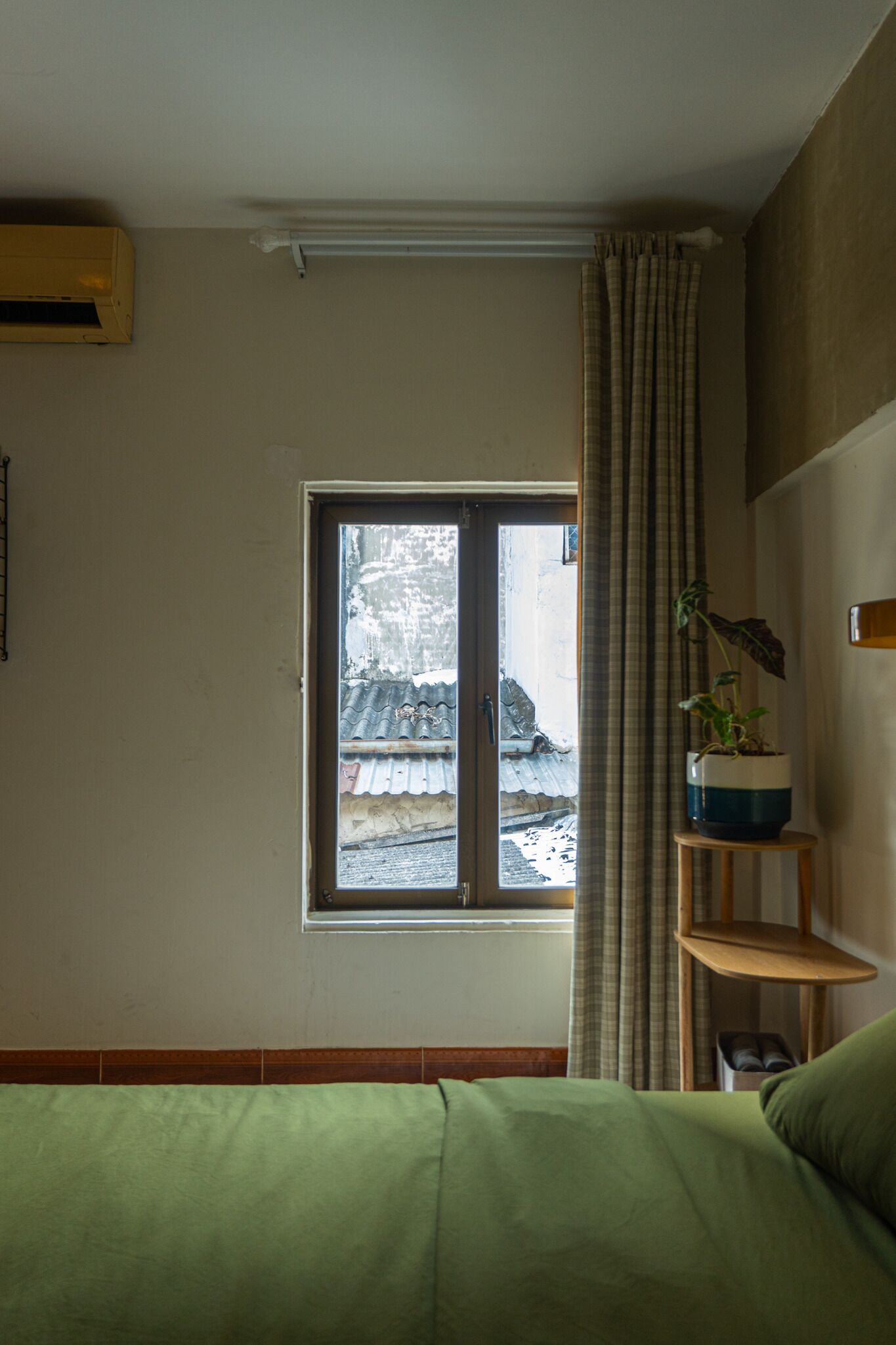 A room with a bed, a window, a potted plant, and a wall-mounted air conditioner.