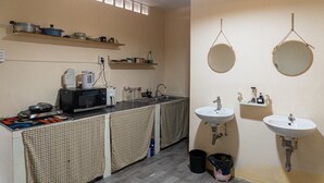 Eine kleine Küche mit Mikrowelle, Wasserkocher und Regalen über der Arbeitsfläche. Zwei Spülen und ein Spiegel sind an der Wand angebracht.