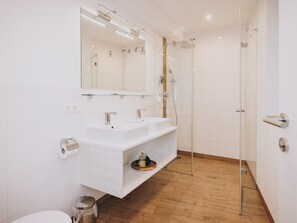 A modern bathroom with a glass shower enclosure, a white sink with a mirror above, and a wooden floor.