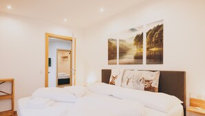 A neatly made bed with white linens and pillows, a bedside table with a lamp, and a wall with three framed pictures depicting nature scenes.