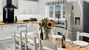 A modern kitchen with white cabinetry, a stainless steel refrigerator, and a dining area set for a meal.