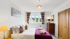 A bedroom with a bed, a window with curtains, a radiator, a wooden wardrobe, and a lamp.