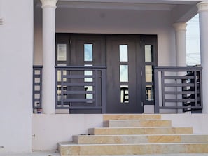 Stunning entrance with a dark door and stone steps, flanked by columns with metal railings.