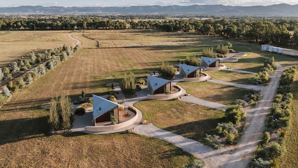 A modern architectural complex with multiple buildings featuring unique roof designs, surrounded by expansive fields and distant mountains. - Oak Studio as Featured in Grand Designs Magazine (Buckaroo)