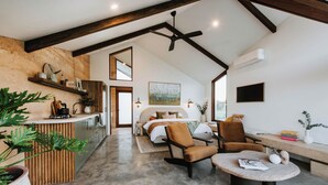 A modern bedroom with a large bed, a desk, and a chair. There is a large window and a ceiling fan.