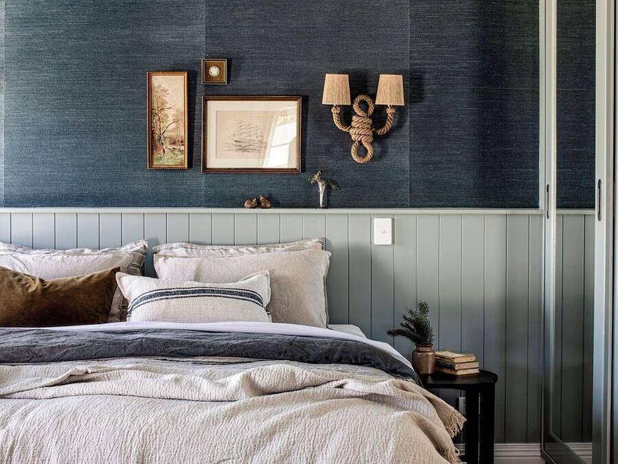 A bedroom with a bed, two wall-mounted lamps, and two framed pictures.