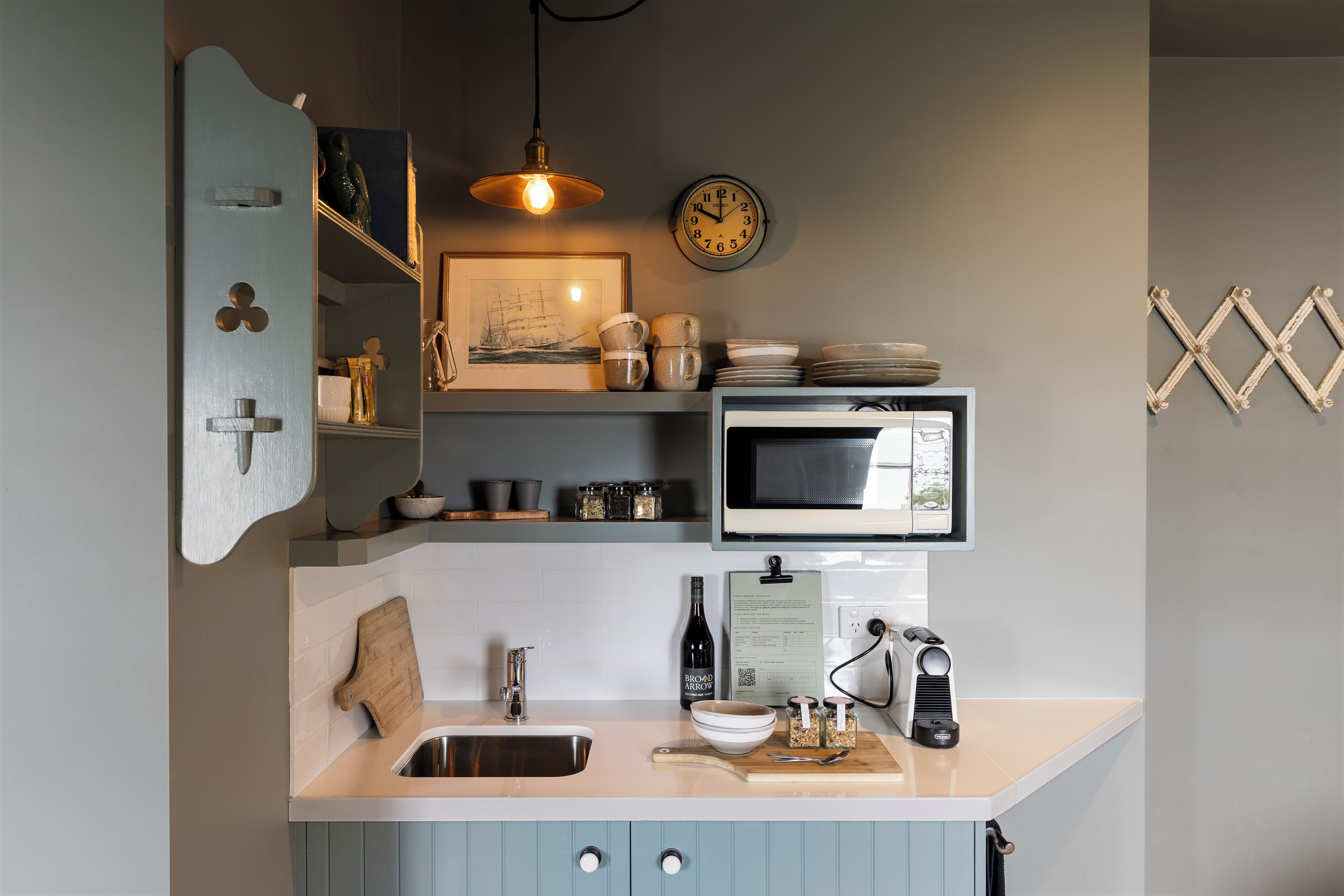 A compact kitchen with a microwave, sink, and wooden cutting board.