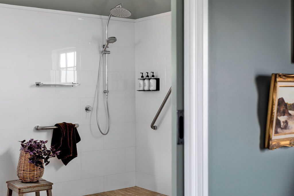 Un baño moderno con ducha, un perchero, un taburete pequeño con una cesta y un cuadro en la pared.