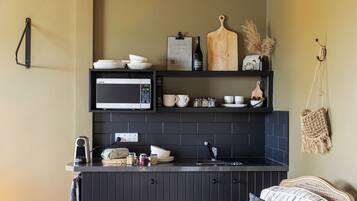 Una cocina con microondas, estantes con vajilla, una tabla de cortar y una bolsa colgada.