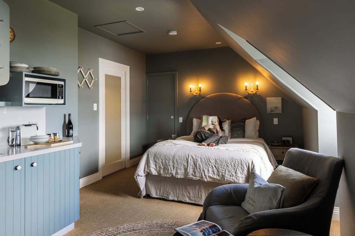 A bedroom with a bed, a chair, a desk, and a microwave.