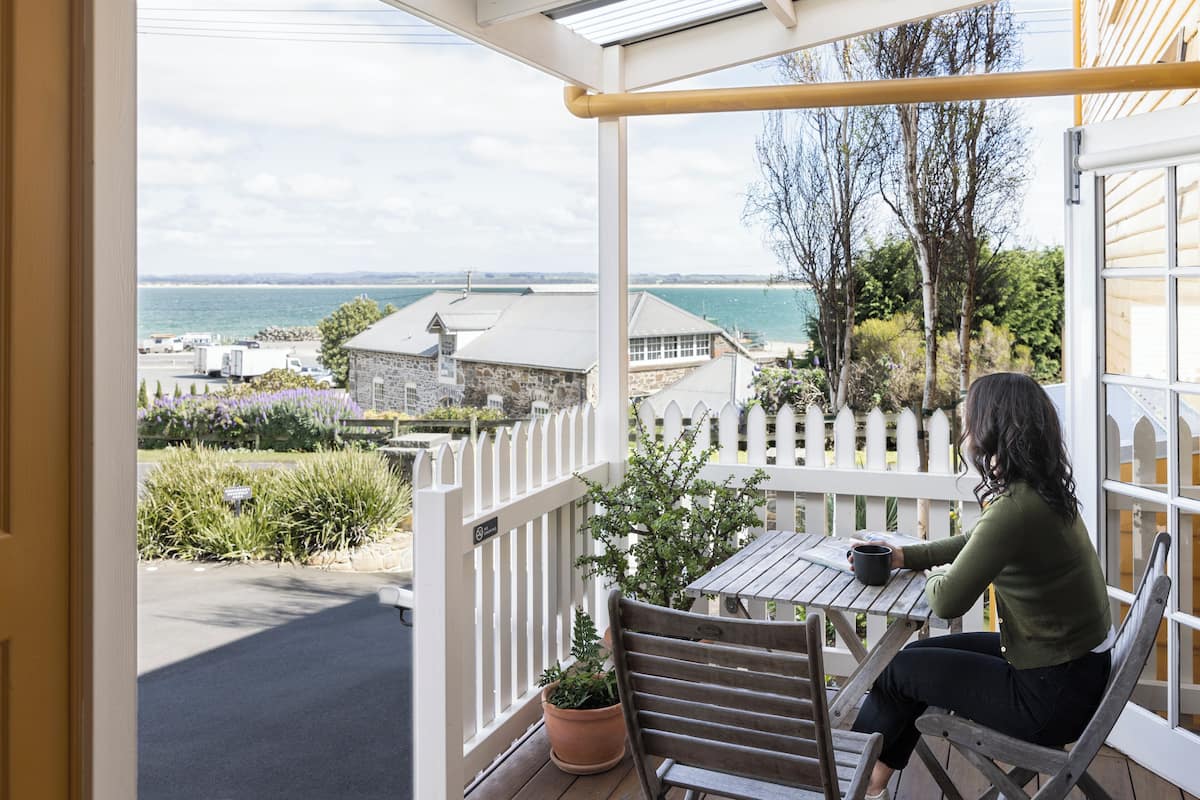 A balcony with a view of the sea, a wooden table, and a potted plant.