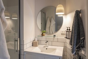 A modern bathroom with a white sink, a round mirror, and a glass shower enclosure.