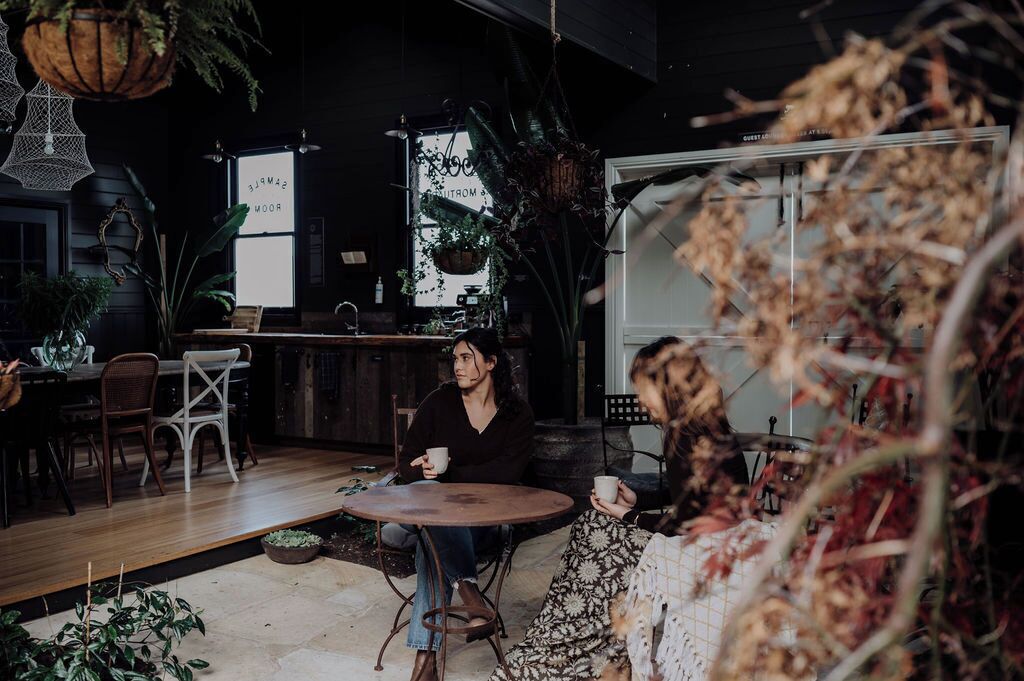 A cozy indoor setting with a wooden table and chairs, surrounded by various plants and hanging decorations.