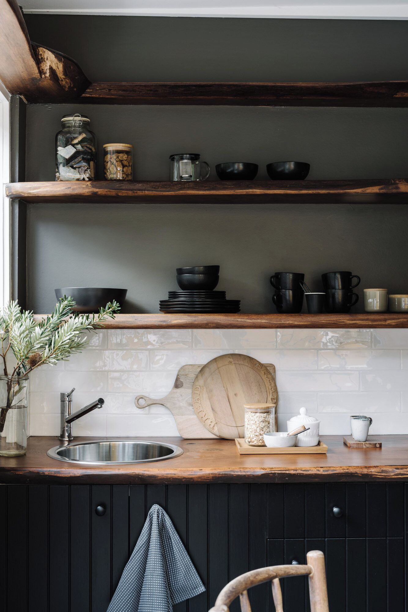 Una cocina con encimera de madera, un fregadero y una tabla de cortar de madera. Hay estantes sobre la encimera con varios utensilios de cocina.