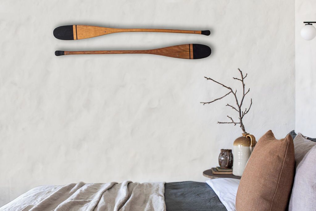 A bedroom with a bed, pillows, a vase with branches, and two wooden paddles on the wall.