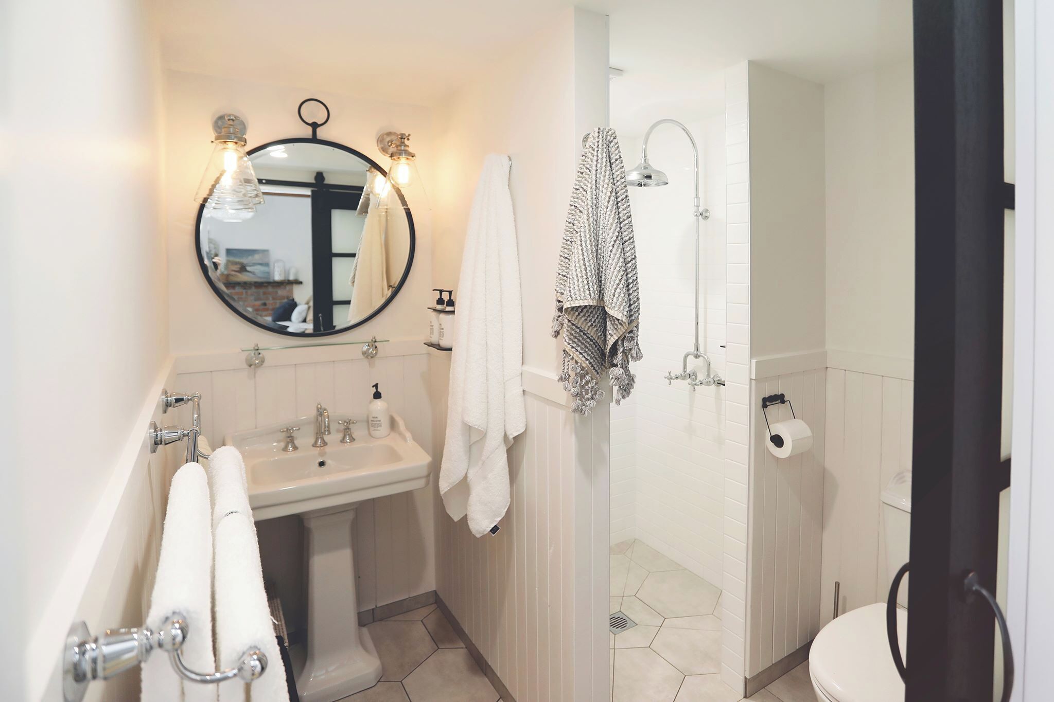 A bathroom with a sink, mirror, towel rack, and shower.