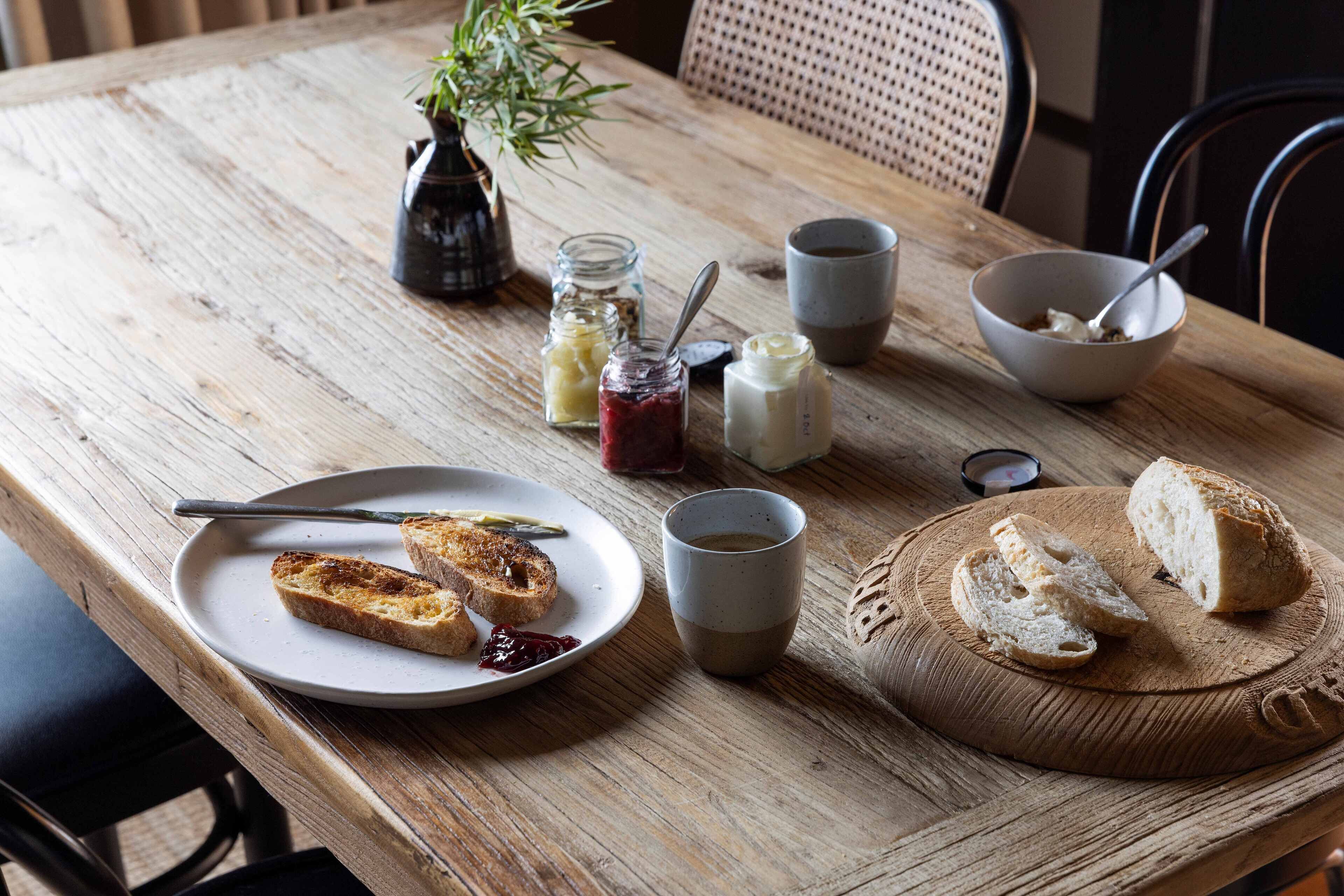 A wooden table with a plate of toast, a cup of coffee, and a bowl of cereal.