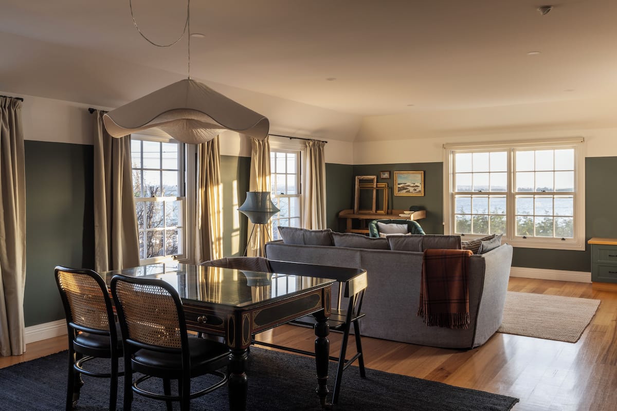 A dining area with a glass table and chairs, a sofa, and a view of the outdoors through large windows.