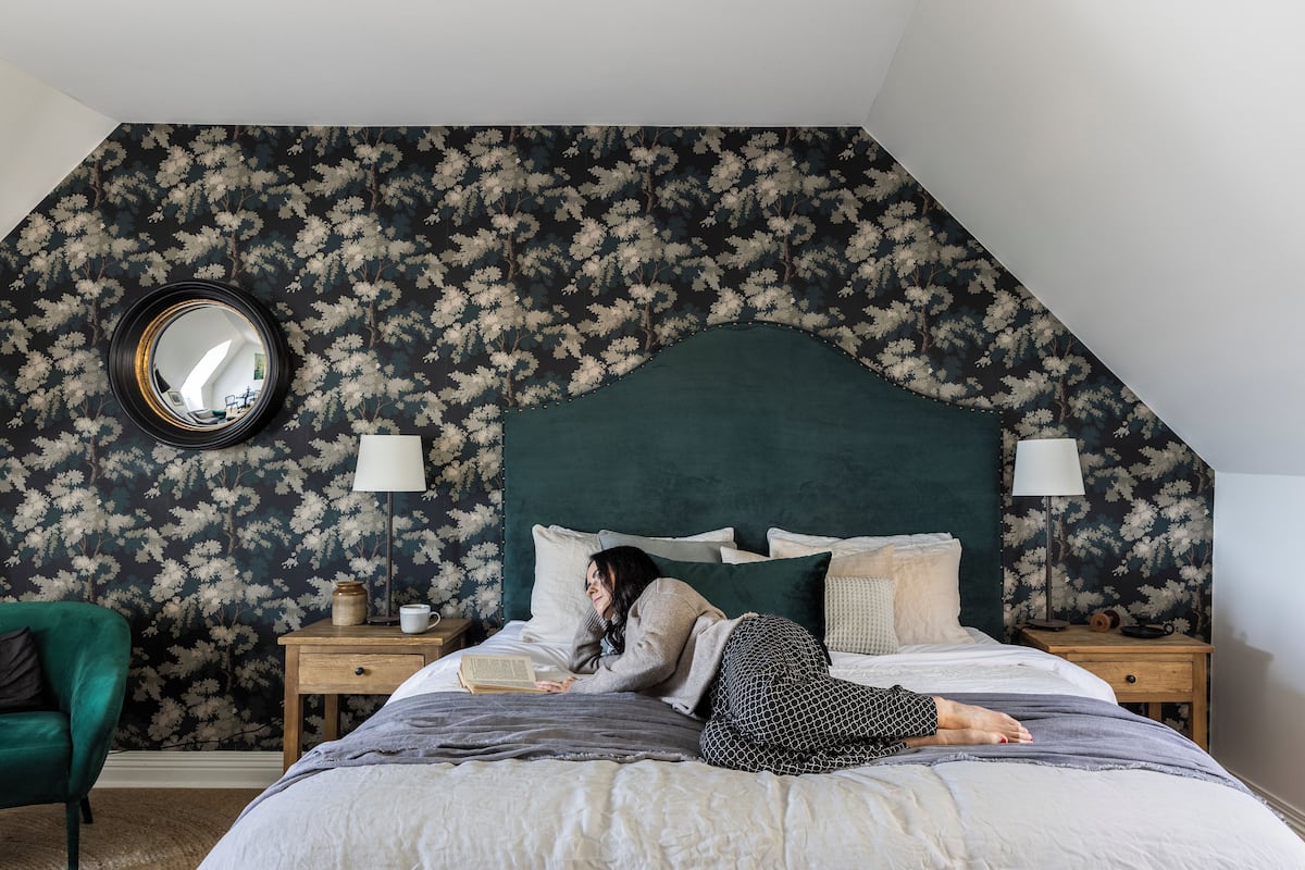 A bedroom with a large bed, two bedside tables, a mirror, and a green armchair.