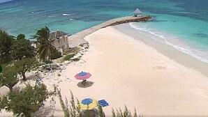 A beach with clear turquoise water, a few umbrellas, and a small structure on the shore.