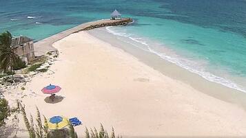 A beach with clear turquoise water, a few umbrellas, and a small structure on the shore.