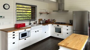 A modern kitchen with white cabinetry, a wooden countertop, a stainless steel refrigerator, and a window with blinds. - Grand View Luxury Villa (Kangaroo Valley)