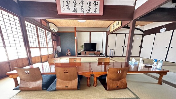 Une pièce de style japonais traditionnel, avec un sol recouvert de tatamis, une petite table en bois et un téléviseur posé au fond de la pièce.