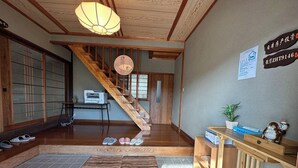 Un intérieur japonais traditionnel avec un escalier en bois, un revêtement de sol en tatami et un comptoir d’accueil agrémenté d’une plante et d’une statuette de singe en céramique.