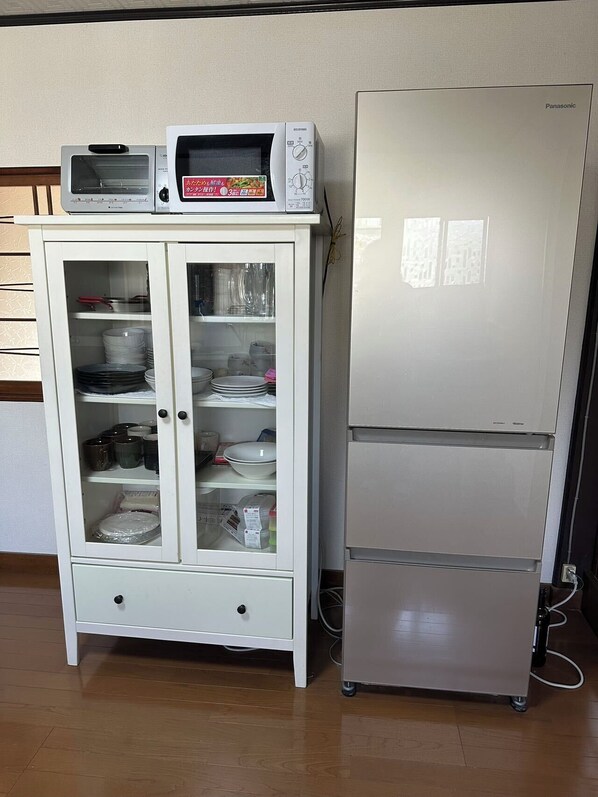 A white cabinet with glass doors containing dishes and a microwave on top. Next to it is a white refrigerator with a control panel on the door. - sun teien (Himeji)