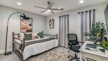 Een slaapkamer met een bed, bureau, stoel, plafondventilator en kunstwerk.