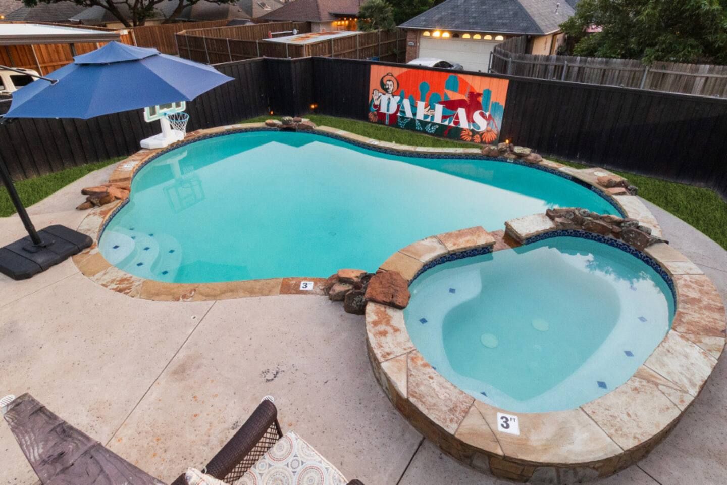 Ein Garten mit Swimmingpool, zwei Whirlpools, einem Sonnenschirm und einem Wandbild.