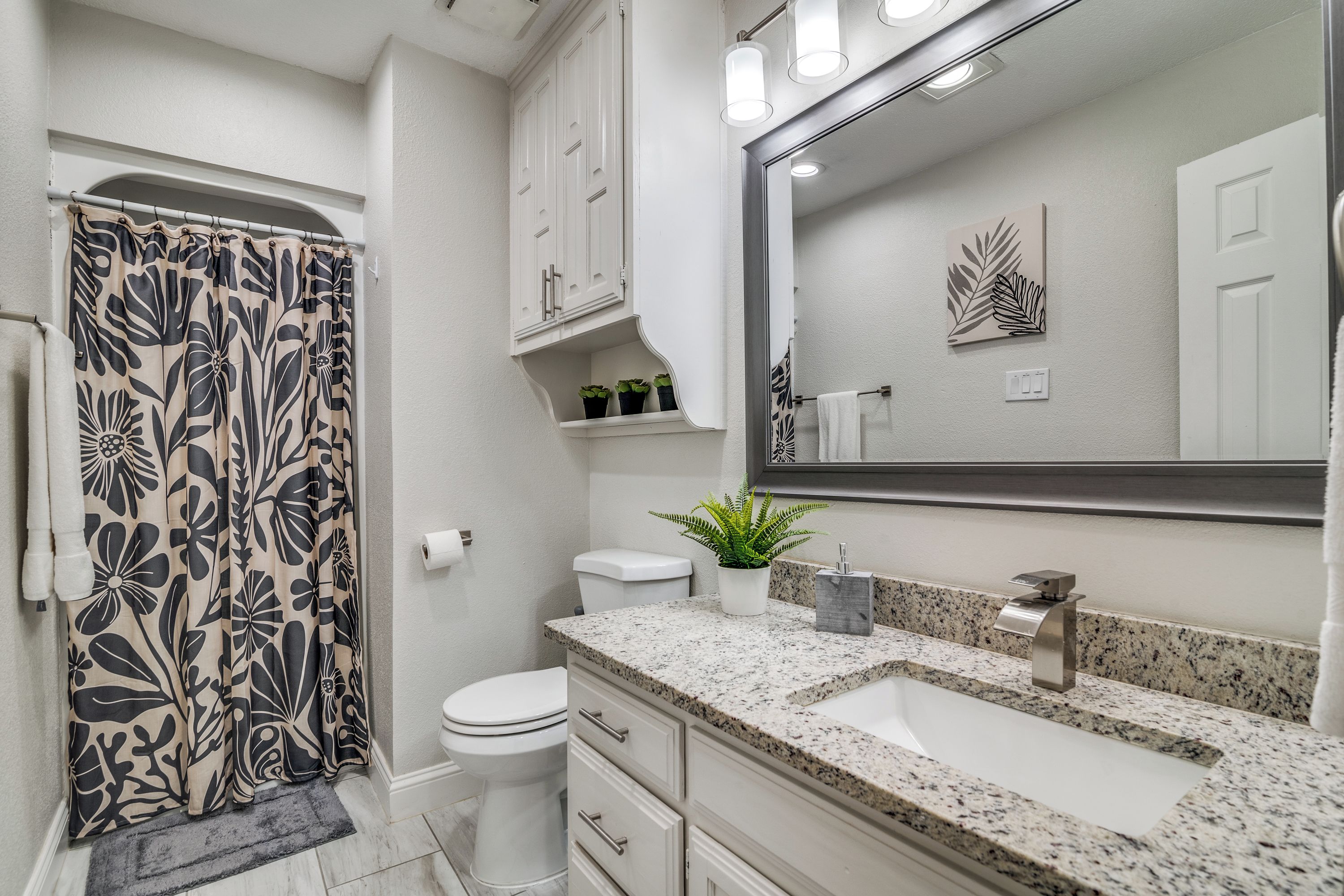 A modern bathroom with a shower curtain, toilet, sink, and mirror.