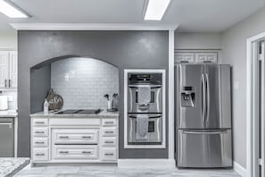Una cocina moderna con armarios blancos, horno empotrado, refrigerador de acero inoxidable y encimera de mármol.