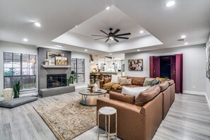 Una sala de estar moderna con chimenea, un sofá grande de cuero marrón, una mesa de centro y un ventilador de techo.