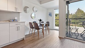 A modern kitchen with white cabinets, a dining area with a glass table and chairs, and a large sliding glass door leading to an outdoor patio. - Modern Studio Steps to UW (Seattle)
