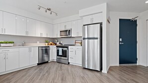 A modern kitchen with white cabinets, stainless steel appliances, and a wooden floor. - Modern Studio Steps to UW (Seattle)