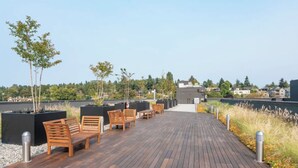 A rooftop deck with wooden benches and tables, surrounded by planters and a view of the city. - Modern Studio Steps to UW (Seattle)