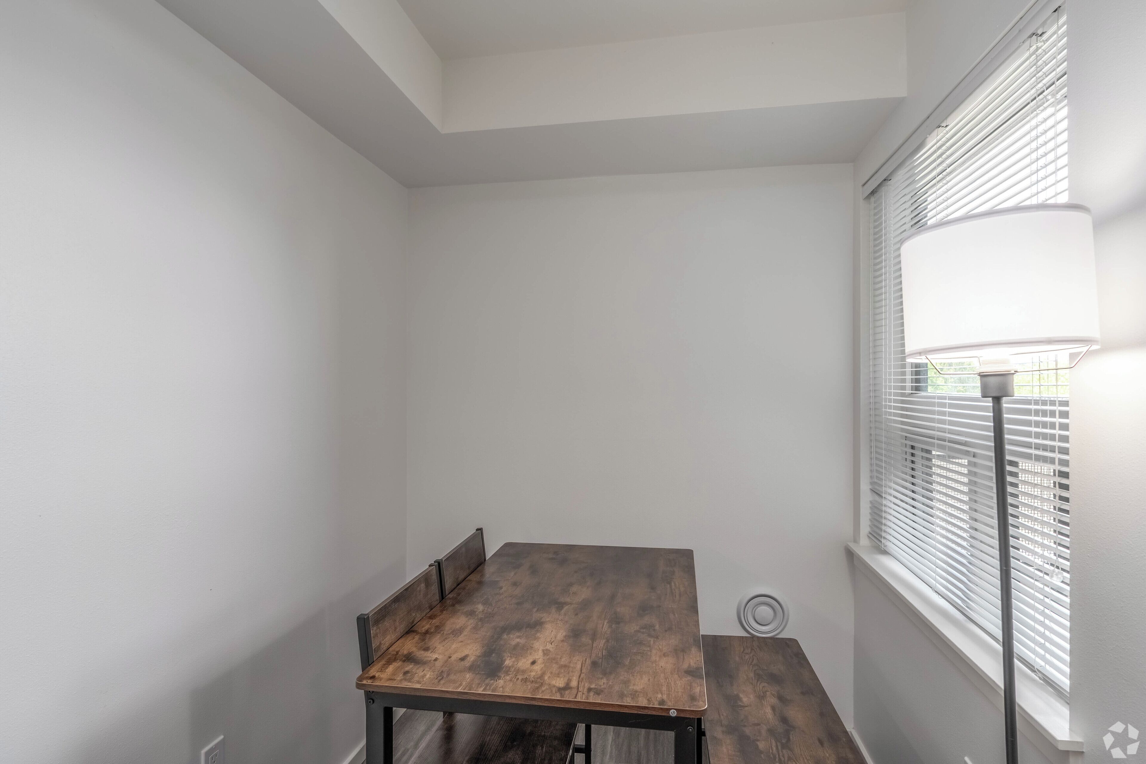 Une pièce avec une table en bois, des murs blancs et une fenêtre avec des stores.