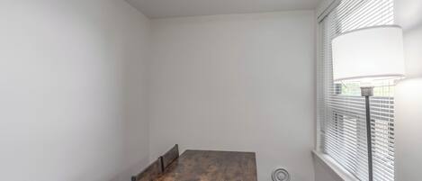 Une pièce avec une table en bois, des murs blancs et une fenêtre avec des stores.