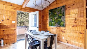 A wooden interior with a dining table set for four, a chandelier, and a large window with a view of trees. - Check out Mossy Fern!! A Cozy Cabin in the Woods in Townsend, TN. (Townsend)