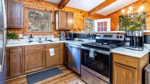 A cabin-style kitchen with wooden walls, a stainless steel stove, and a coffee maker. - Check out Mossy Fern!! A Cozy Cabin in the Woods in Townsend, TN. (Townsend)