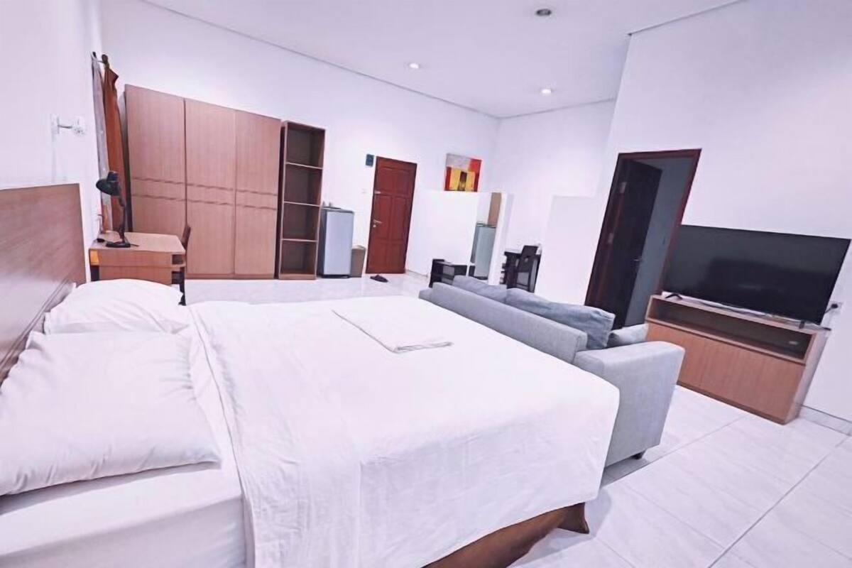 A modern bedroom with a large bed, a sofa, a TV, and a wardrobe.