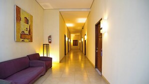 A hotel corridor with a sofa, a painting, and a hallway leading to a door. - Jambuluwuk Mansion Pakubuwono (Jakarta)