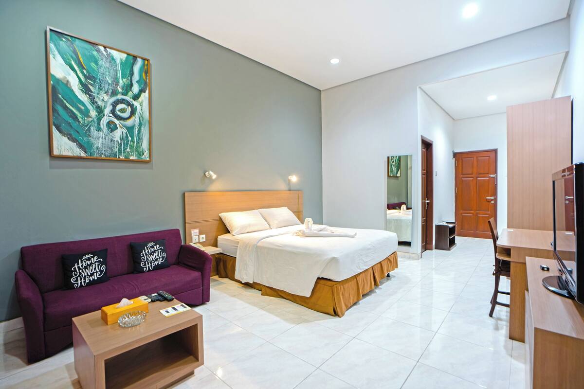 A modern hotel room with a bed, a sofa, a coffee table, a TV, and a painting on the wall.