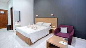A modern hotel room with a large bed, a wooden headboard, a purple armchair, and a small table with a remote control. - Jambuluwuk Mansion Pakubuwono (Jakarta)