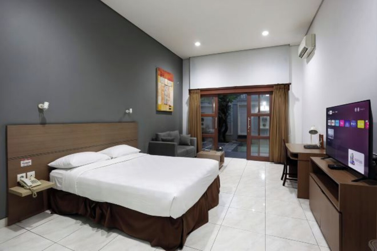 A hotel room with a large bed, a desk, a television, and a view of the outside.